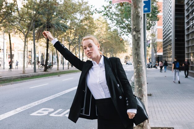 Front view of young businesswoman standing on the road hailing a cab taxi