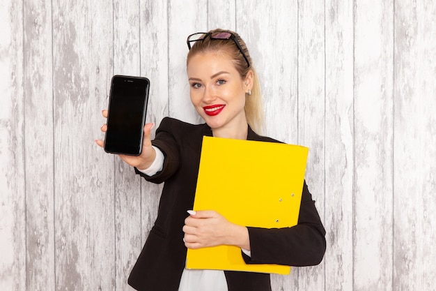 Front view young businesswoman in strict clothes black jacket holding documents and phone on white surface