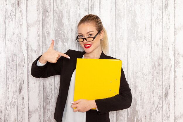 Front view young businesswoman in strict clothes black jacket holding files and documents smiling on white surface