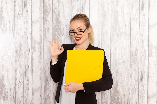 Front view young businesswoman in strict clothes black jacket holding files and documents on the white desk