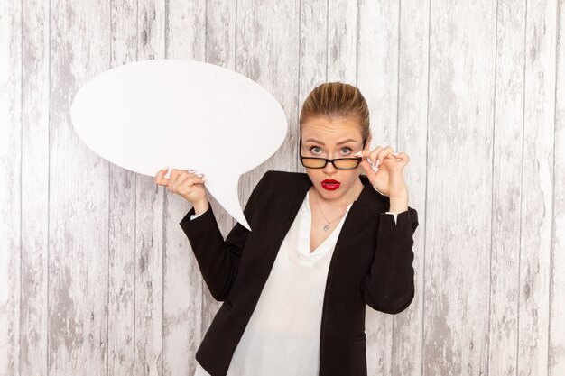 Front view young businesswoman in strict clothes black jacket holding huge white sign on the white surface