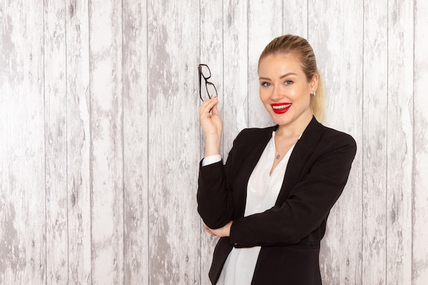 Front view young businesswoman in strict clothes black jacket posing and smiling on white surface