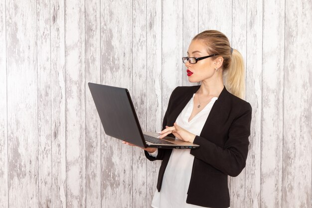 Front view young businesswoman in strict clothes black jacket using her laptop on white surface