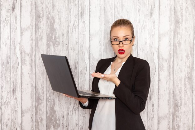 Front view young businesswoman in strict clothes black jacket using laptop on the white desk work job office business