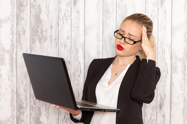 Vista frontale giovane imprenditrice in abiti rigorosi giacca nera utilizzando il computer portatile sul muro bianco lavoro lavoro ufficio donna lavoratore di affari