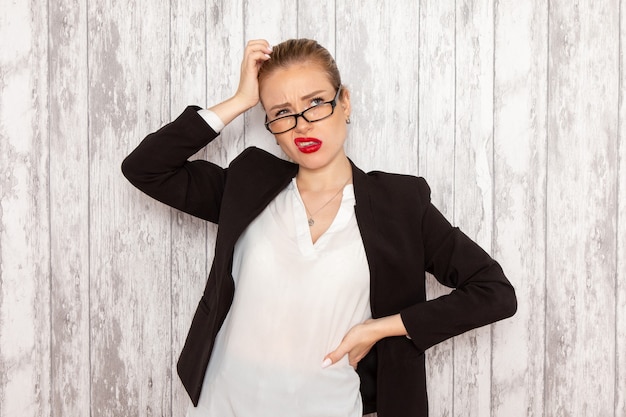 Front view young businesswoman in strict clothes black jacket with optical sunglasses posing thinking on white desk work job office business woman lady