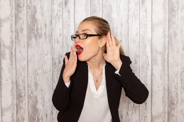 Front view young businesswoman in strict clothes black jacket with optical sunglasses trying to hear on white desk work job office female business