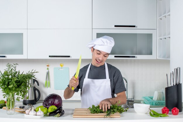 Front view young chef in uniform enjoying cutting greens