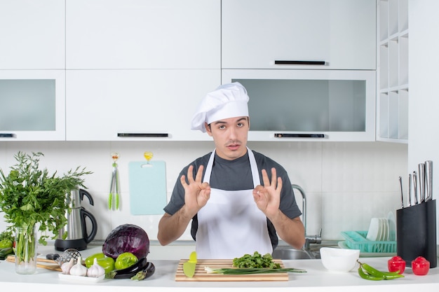 Giovane chef di vista frontale in uniforme che fa segno okey in cucina