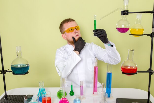 Front view young chemist looking at green chemical in orange colour protective glasses