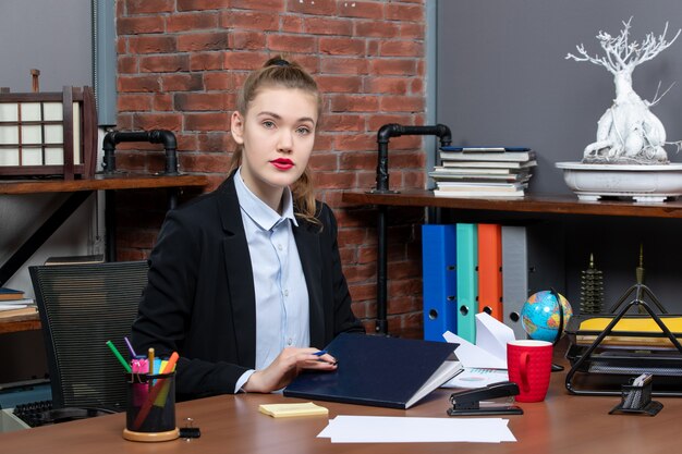 Front view of young confident female assistant sitting at her desk in the office