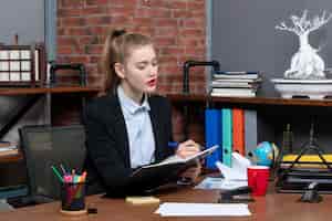 Free photo front view of young confident female assistant sitting at her desk and writing her document in the office