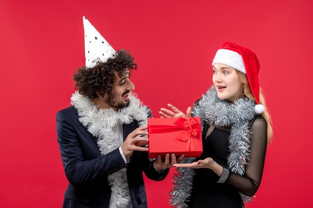 赤い床のクリスマスの愛のパーティーで祝うプレゼントと正面図の若いカップル