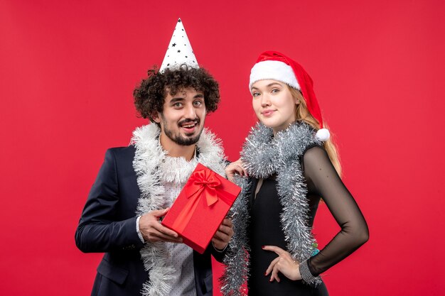 赤い壁のクリスマスの愛のパーティーを祝うプレゼントと正面図の若いカップル