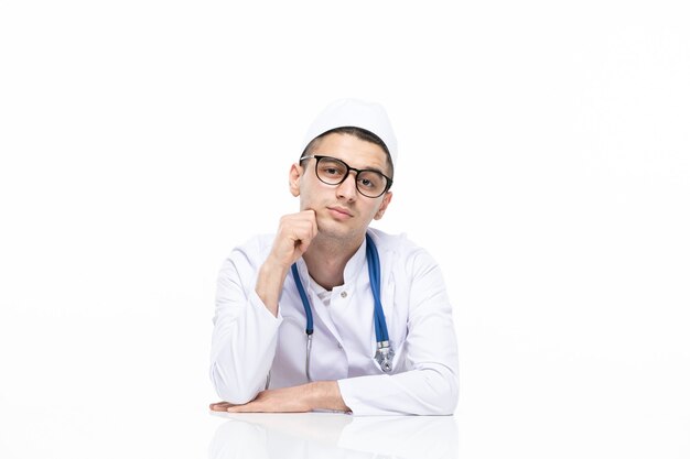 Вид спереди молодой врач в медицинском костюме, сидя за столом