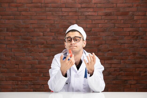 Front view young doctor in white medical suit holding empty little flask