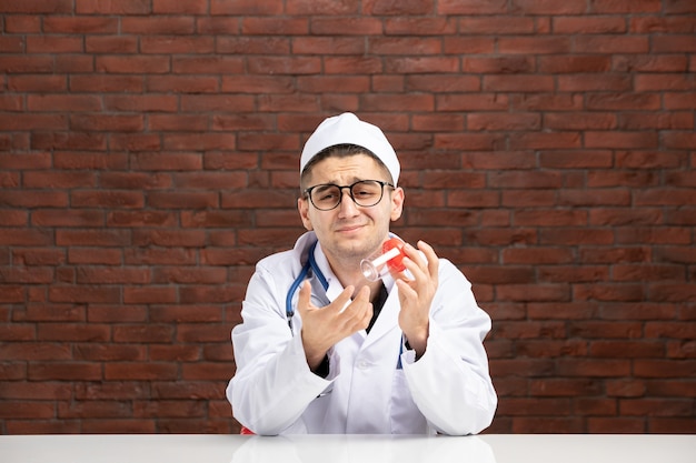 Вид спереди молодой врач в белом медицинском костюме, держащий пустую фляжку