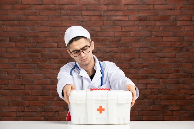 Front view young doctor in white medical suit with first aid kit