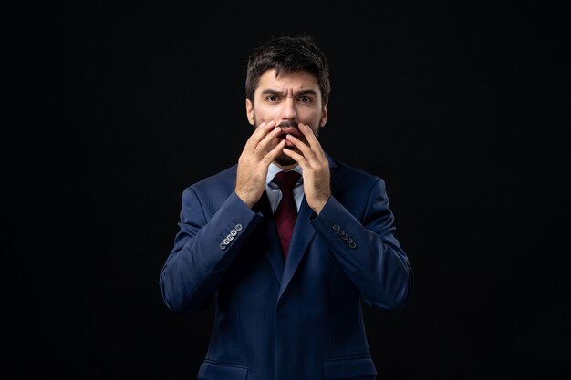 Front view of young emotional shocked man in suit on isolated dark wall