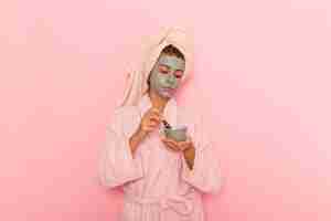 Бесплатное фото Вид спереди молодая женщина после душа в розовом халате, применяющая маску на розовом полу, ванна, душ, водный крем, девушка красоты