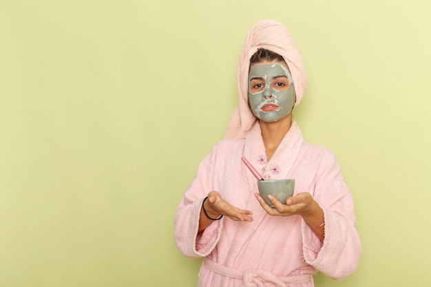 녹색 표면에 마스크를 적용하는 분홍색 목욕 가운에 샤워 후 전면보기 젊은 여성