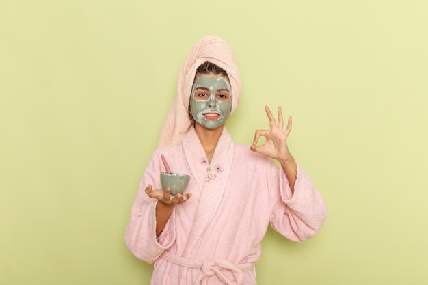 녹색 표면에 마스크와 그릇을 들고 분홍색 목욕 가운에 샤워 후 전면보기 젊은 여성
