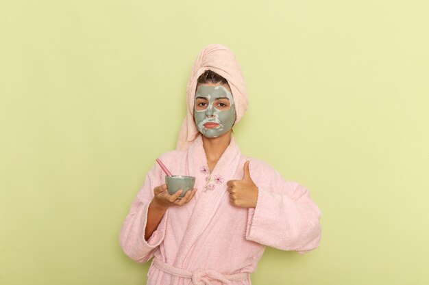Free photo front view young female after shower in pink bathrobe holding bowl with mask on a green surface