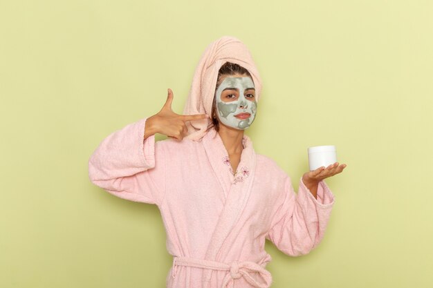Front view young female after shower in pink bathrobe holding cream on green surface