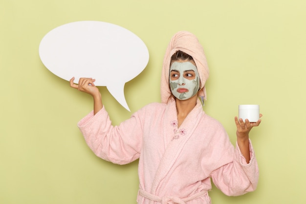 Free photo front view young female after shower in pink bathrobe holding cream and white sign on green desk