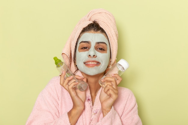 Front view young female after shower in pink bathrobe holding make-up remover on green surface