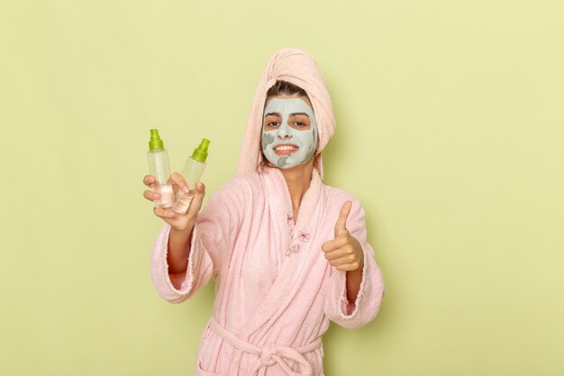 Front view young female after shower in pink bathrobe holding make-up removers on a green surface