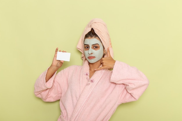 Front view young female after shower in pink bathrobe holding white card on green surface