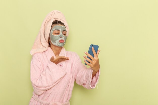 녹색 표면에 그녀의 전화를 사용하여 분홍색 목욕 가운에 샤워 후 전면보기 젊은 여성