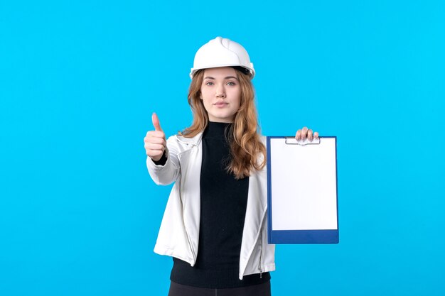 Вид спереди молодая женщина-архитектор в шлеме на синем