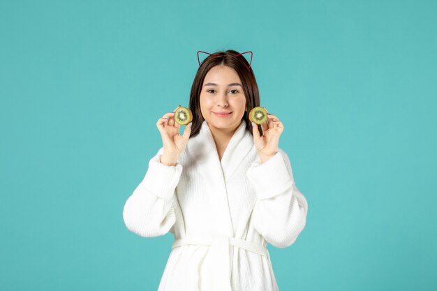 front view young female in bathrobe holding sliced kiwis on blue background