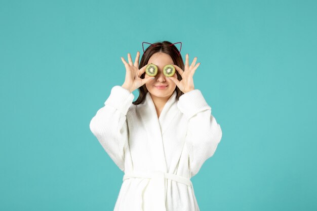 front view young female in bathrobe holding sliced kiwis on blue background