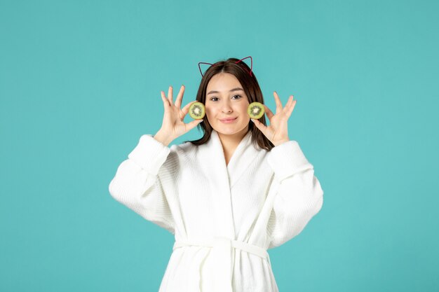 front view young female in bathrobe holding sliced kiwis on blue background