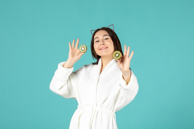 front view young female in bathrobe holding sliced kiwis on blue background