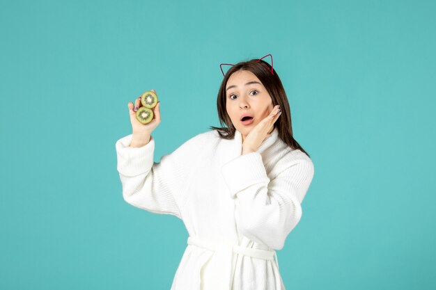 front view young female in bathrobe holding sliced kiwis on blue background