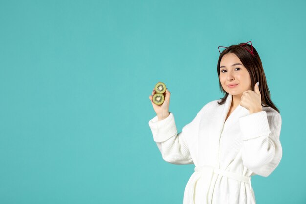 front view young female in bathrobe holding sliced kiwis on blue background