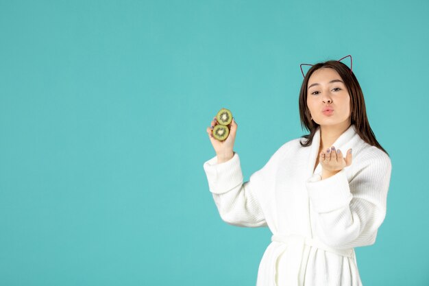 front view young female in bathrobe holding sliced kiwis on blue background