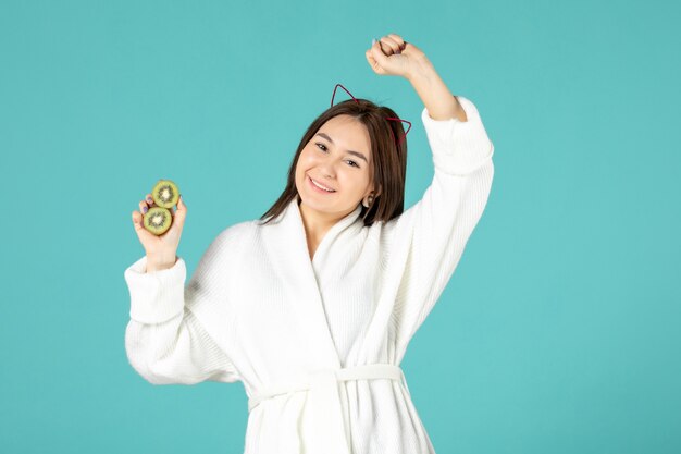 front view young female in bathrobe holding sliced kiwis on blue background