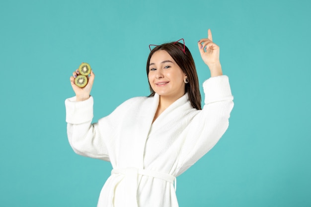 front view young female in bathrobe holding sliced kiwis on blue background