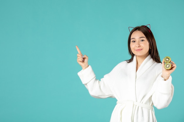 Free photo front view young female in bathrobe holding sliced kiwis on blue background