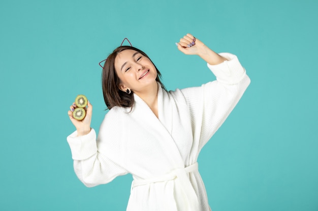 front view young female in bathrobe holding sliced kiwis on blue background