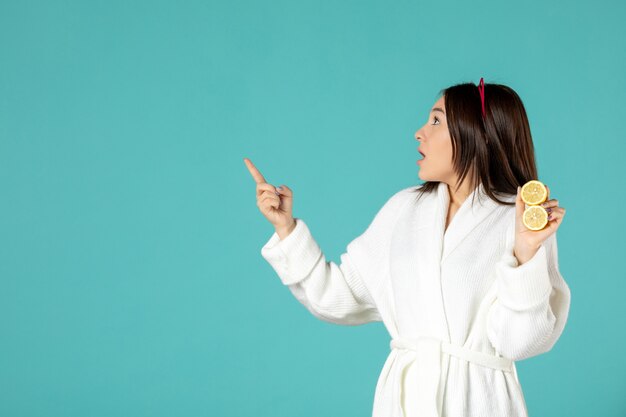 front view young female in bathrobe holding sliced lemons on blue background