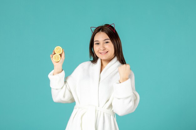 вид спереди молодая женщина в халате держит нарезанные лимоны на синем фоне
