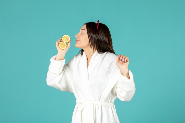 front view young female in bathrobe holding sliced lemons on blue background