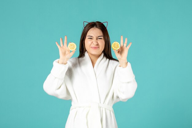 front view young female in bathrobe holding sliced lemons on blue background