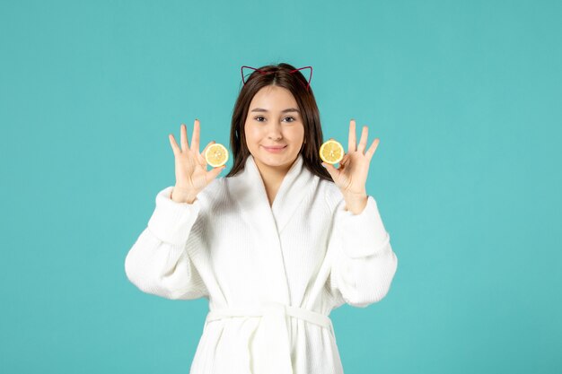 front view young female in bathrobe holding sliced lemons on blue background